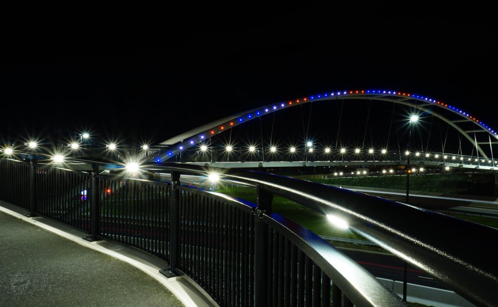 Wyvern Footbridge illuminated by red and blue lights on top and with white lights on handrails.