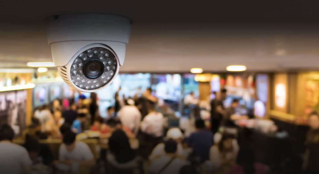 Close up of security camera on the ceiling, above a crowd of people