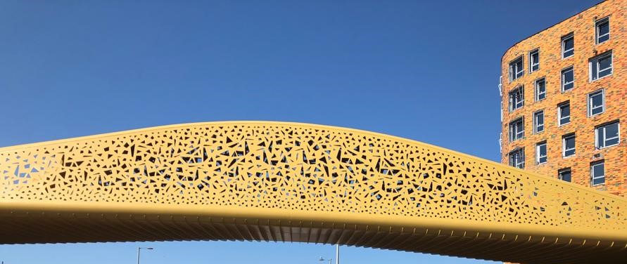 Image of Swansea's Copr Bay Bridge, a copper coloured structure with cut outs to create shapes along both sides.