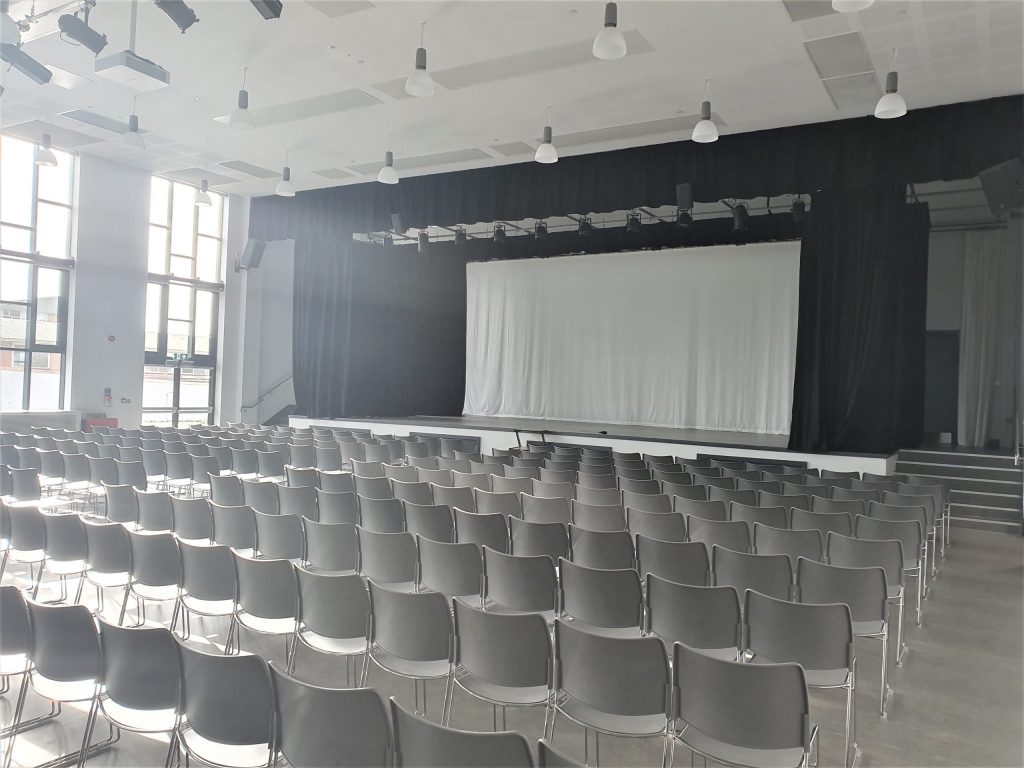 image of a school hall with seats arranged in rows facing a stage with a white curtain