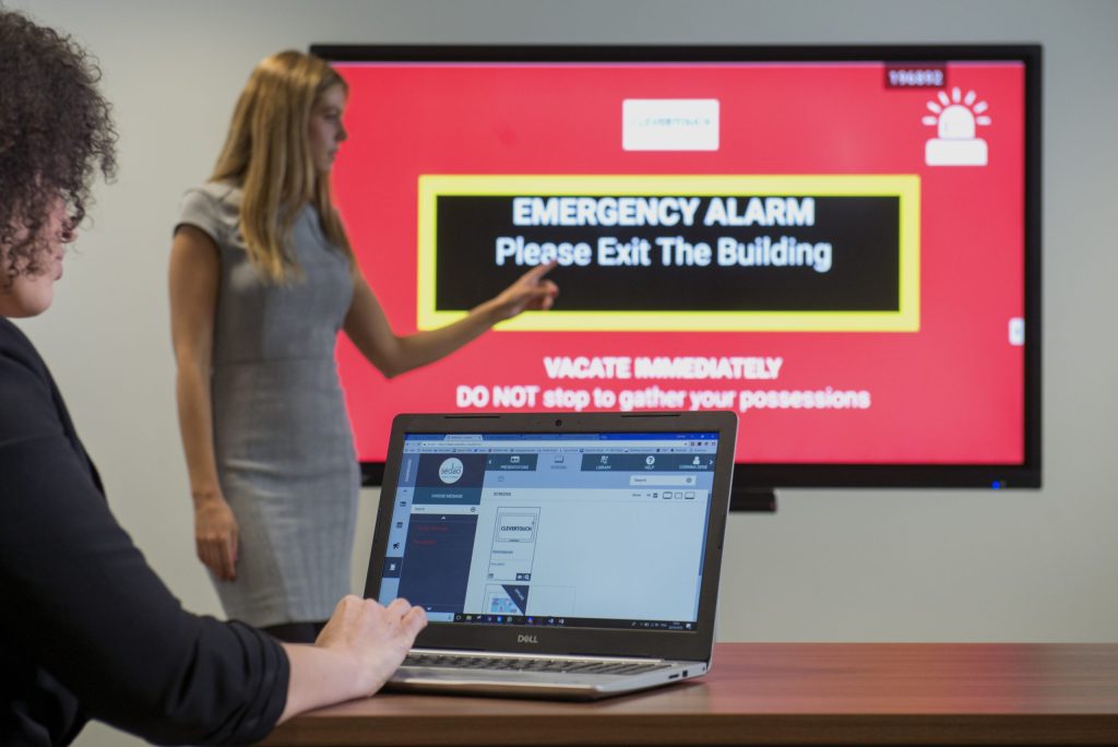 Woman interacting with large display screen, which states what to do when an emergency alarm goes off