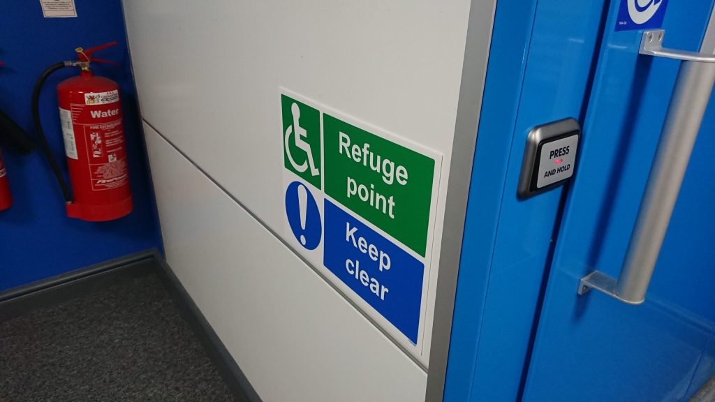 Photo showing disabled refuge signage on a white wall.