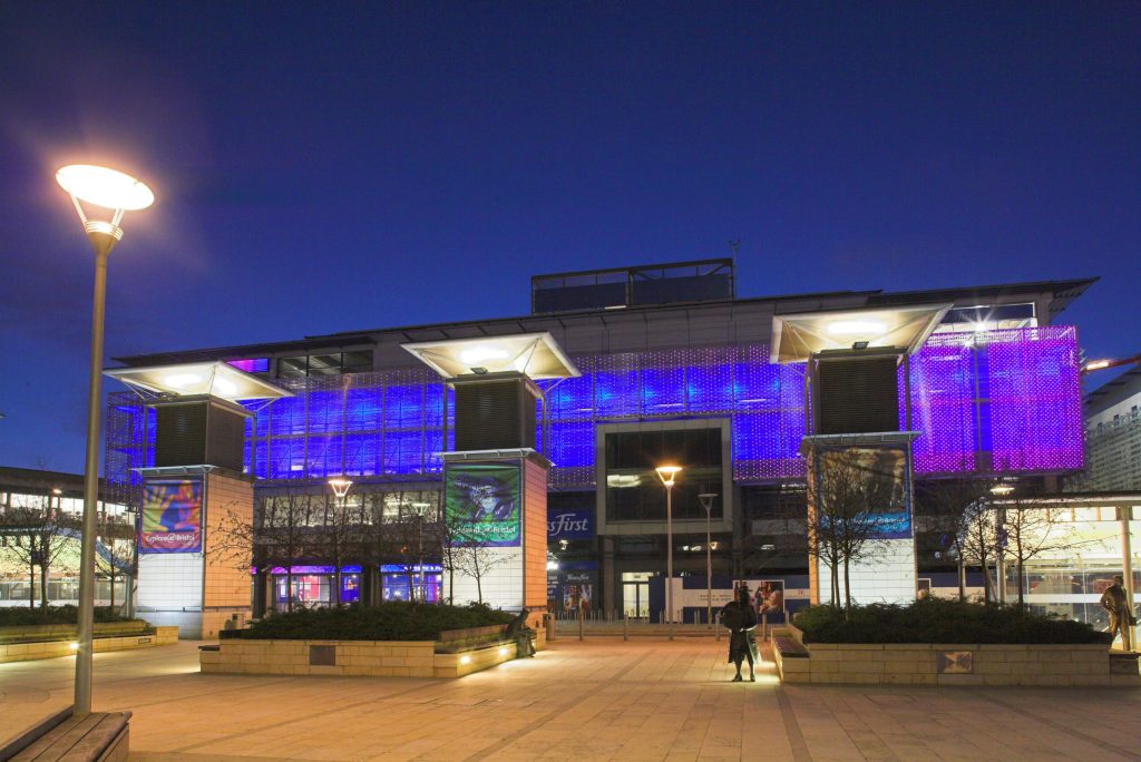 The exterior of a building in the night, lit with blue & purple lights