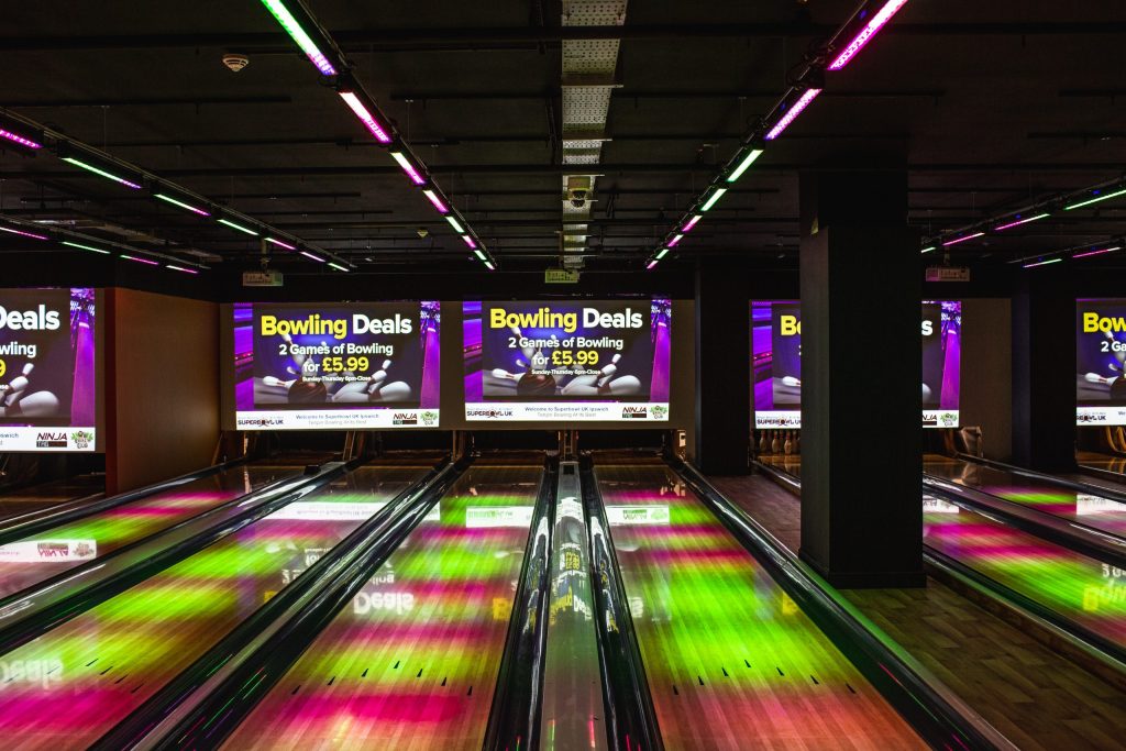 interior of a bowling alley with four lanes, illuminated with green and pink lighting