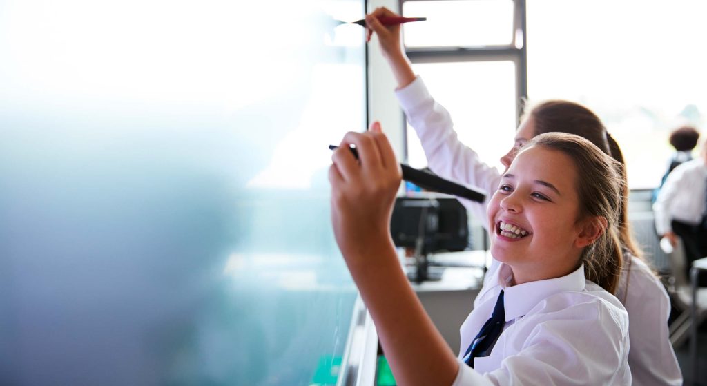 Close up of two school children in a classroom writing on an interactive touchscreen