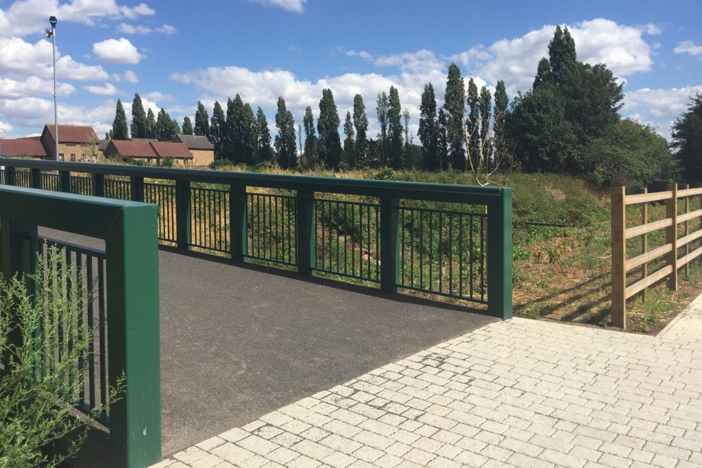 A green bridge next to a tree-lined field