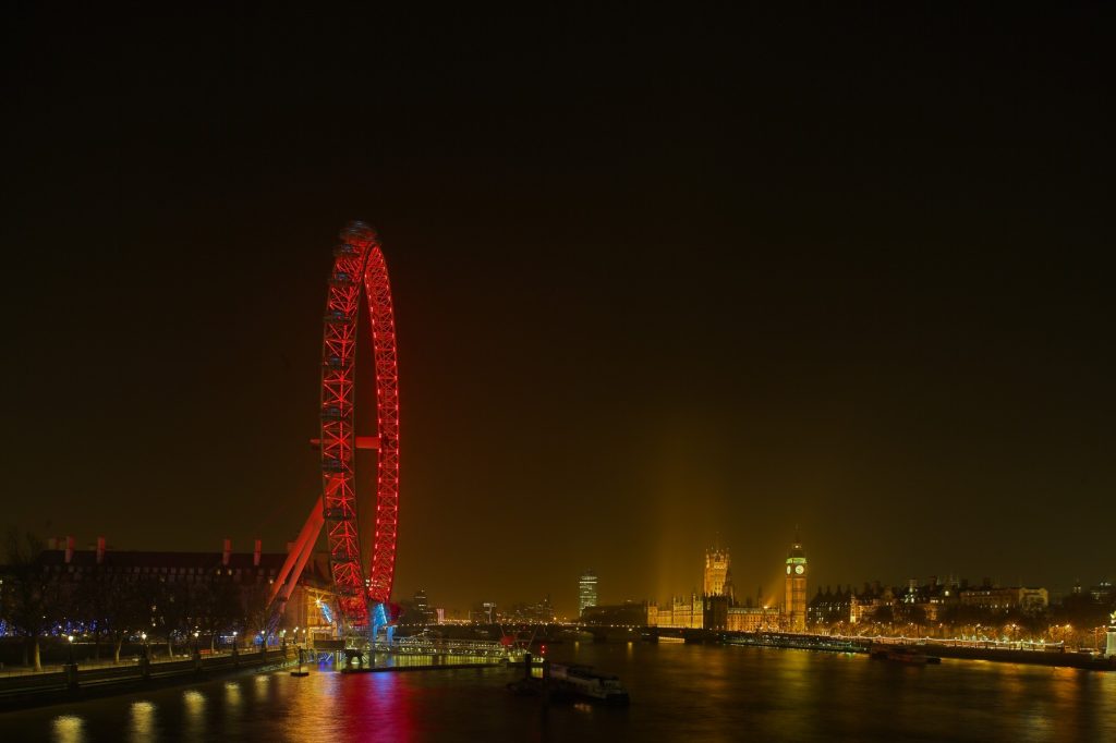 Landscape shot of the River Thames at night, with the London Eye on the left. The London Eye is lit up with red lights