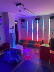 Sensory play room with light tubes against one wall and soft furnishings in the foreground.