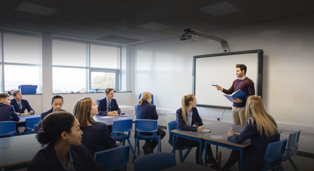 Pupils sitting in a classroom, with a teacher stood up and speaking to them