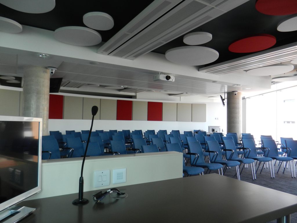 Empty conference room filled with blue seats, with a podium and microphone in the forefront